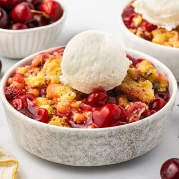 Cherry Cobbler made with a boxed cake mix in a bowl topped by vanilla ice cream.