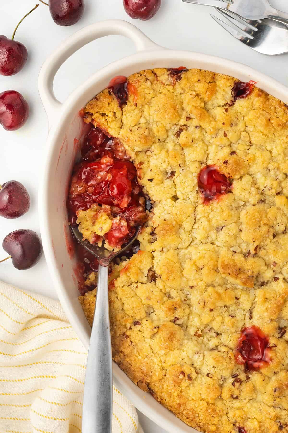 Using a spoon to dish up a serving of cherry cobbler in a baking dish. 