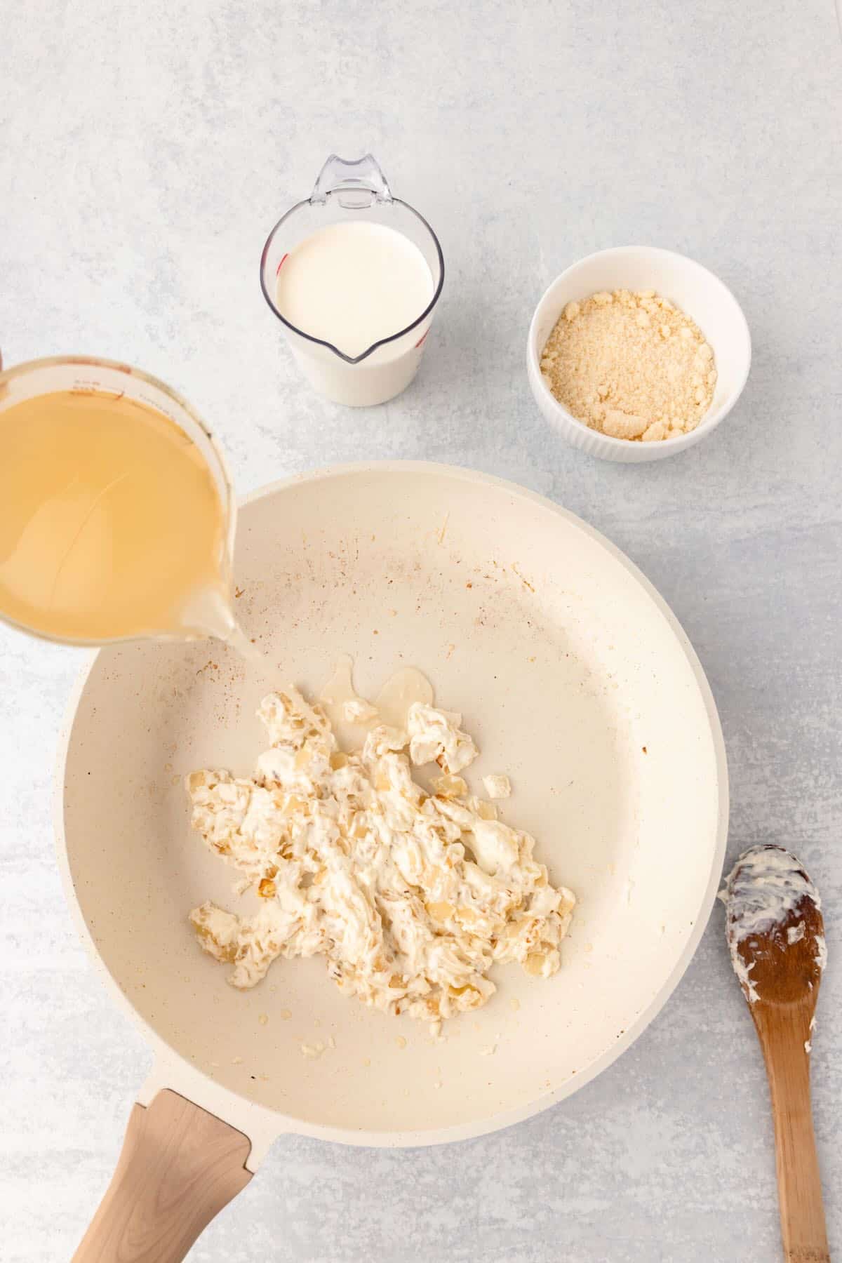 Adding chicken stock to a skillet with cream cheese and onions. 