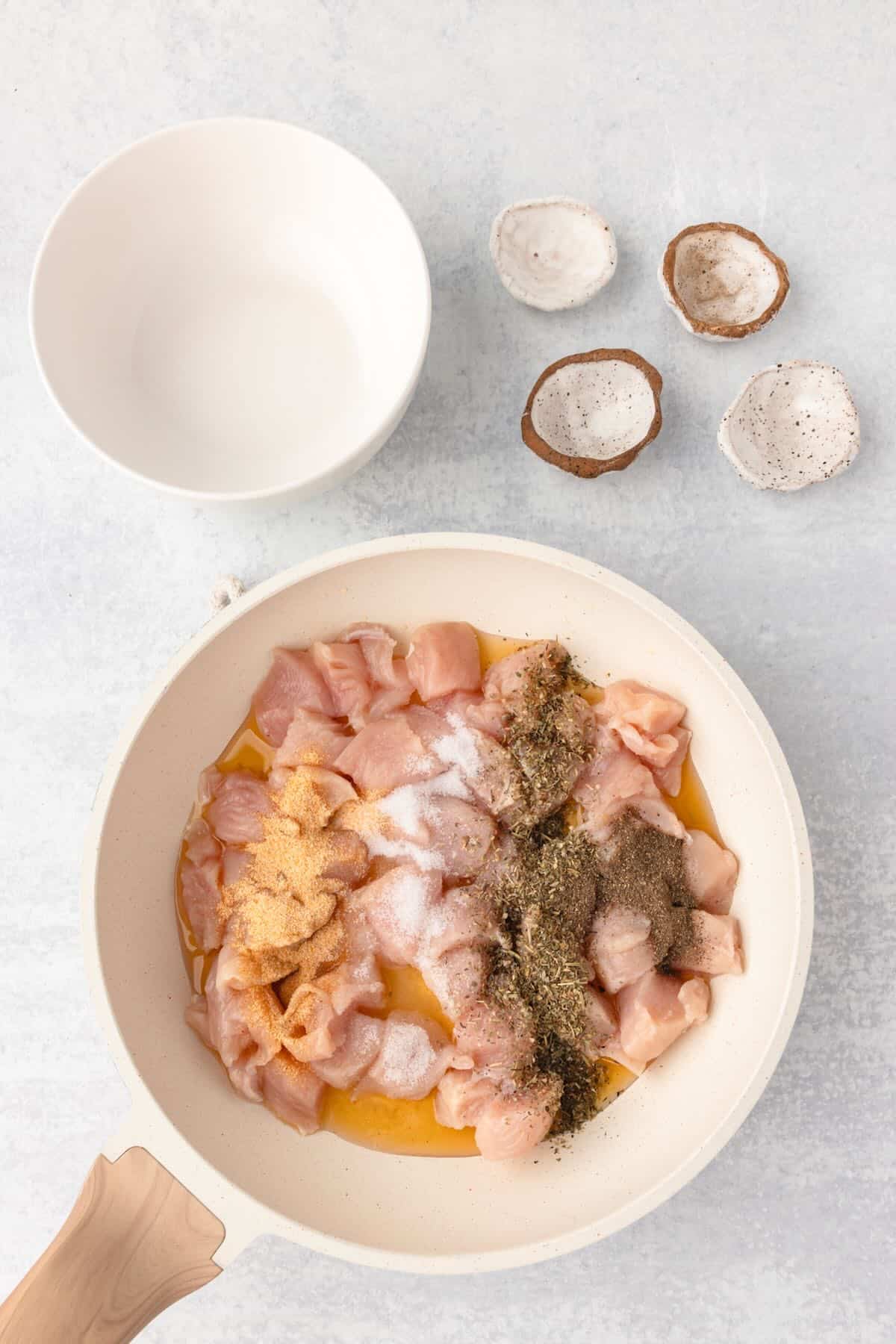 Bite-sized chicken pieces and seasoning in a white skillet. 