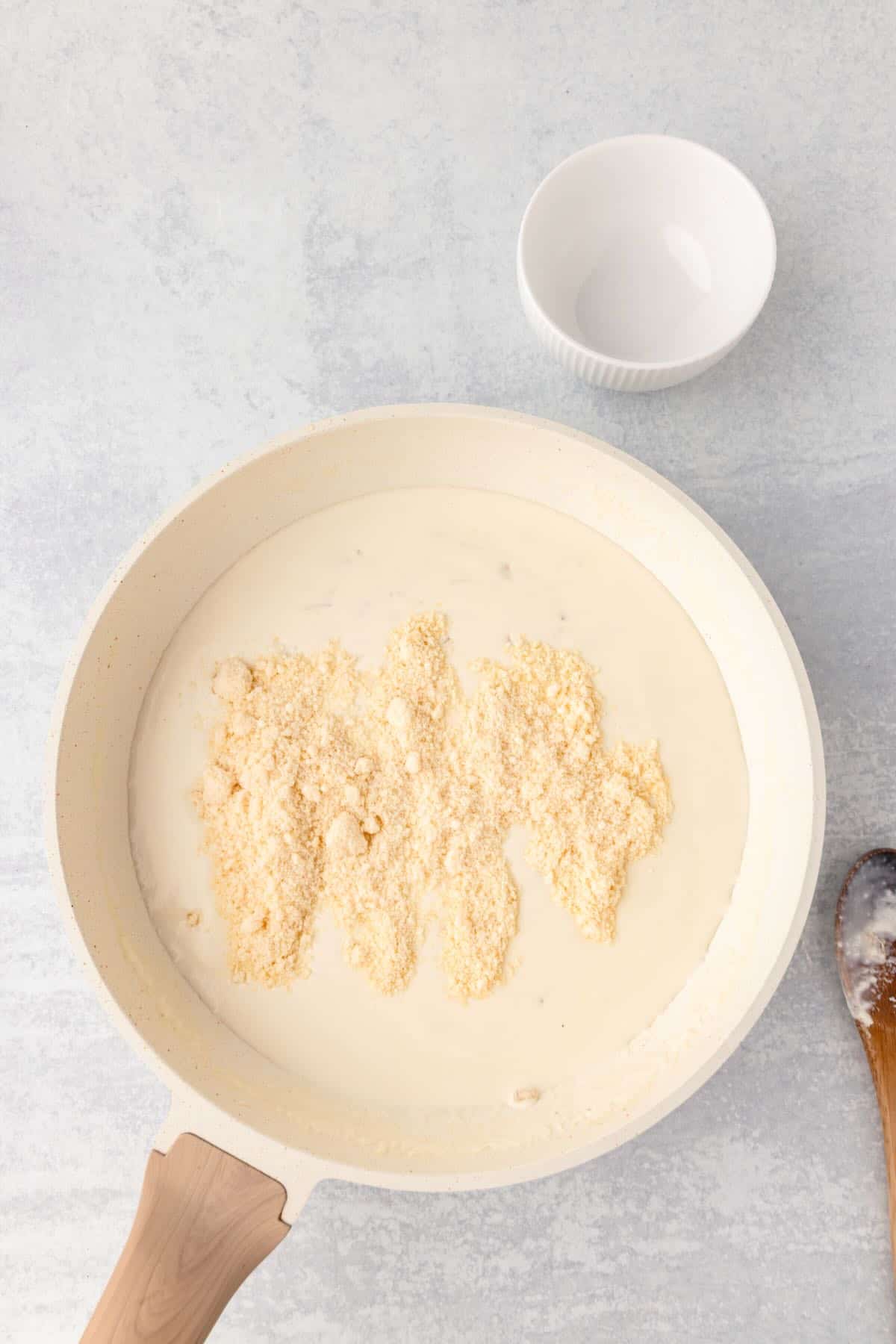 Grated parmesan cheese is added to a cream sauce in a skillet. 