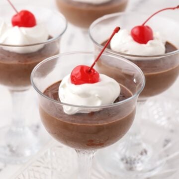 Homemade chocolate pudding made without cornstarch in dessert cups. The pudding is topped with whipped cream and a cherry.