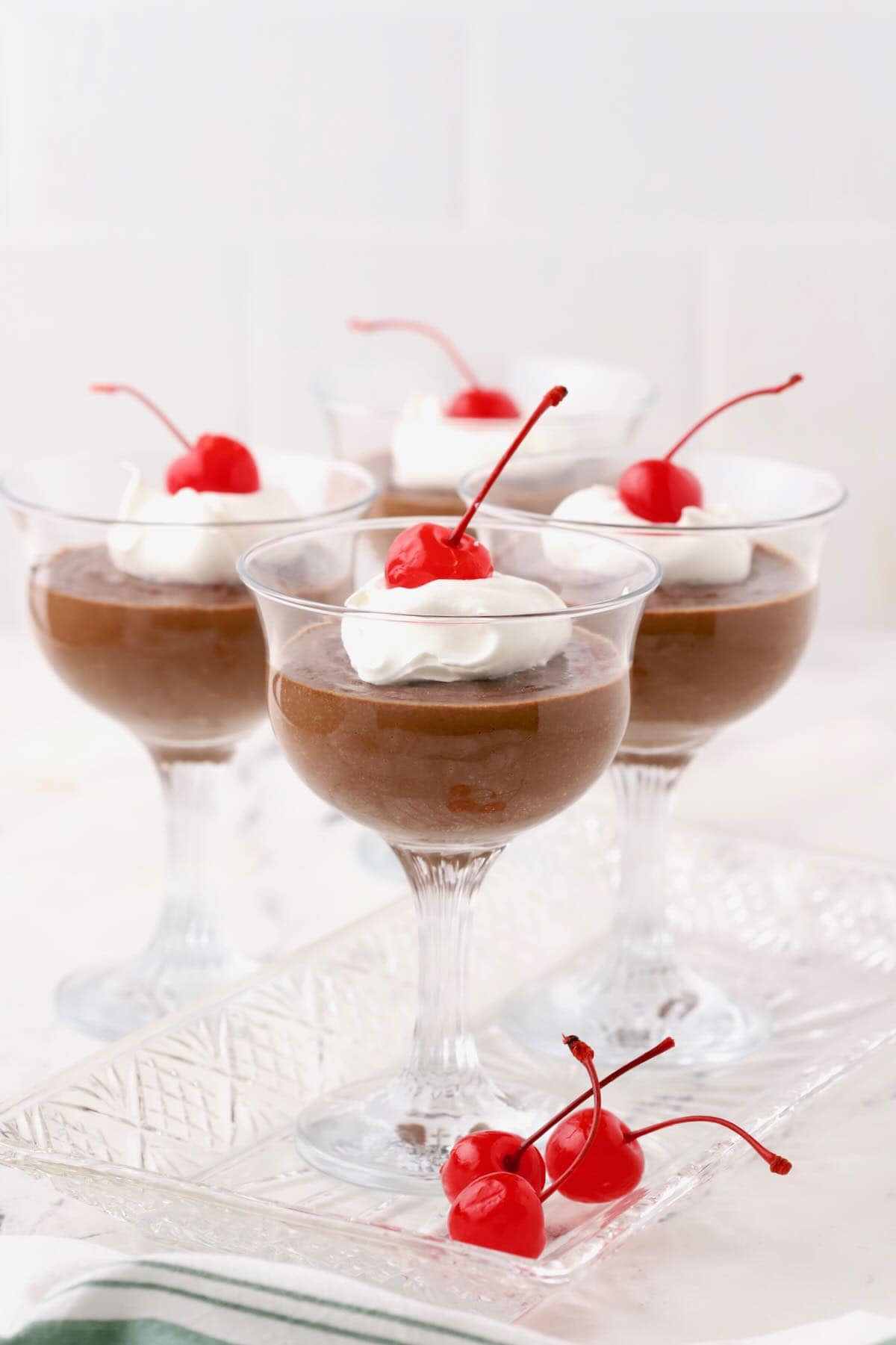 Chocolate pudding in four dessert glasses topped with whipped cream and a cherry. 