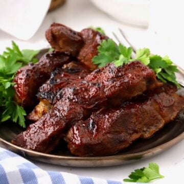 A plate of oven-baked country-style ribs topped with BBQ sauce and garnished with parsley.