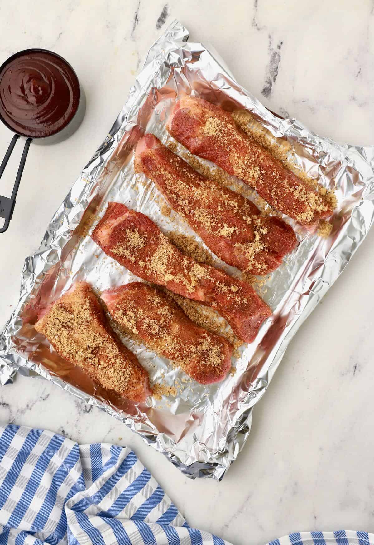 Boneless ribs on a baking sheet topped with a dry rub. 