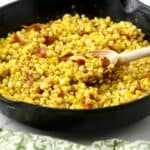 Southern fried corn topped with bacon in a black cast iron skillet.