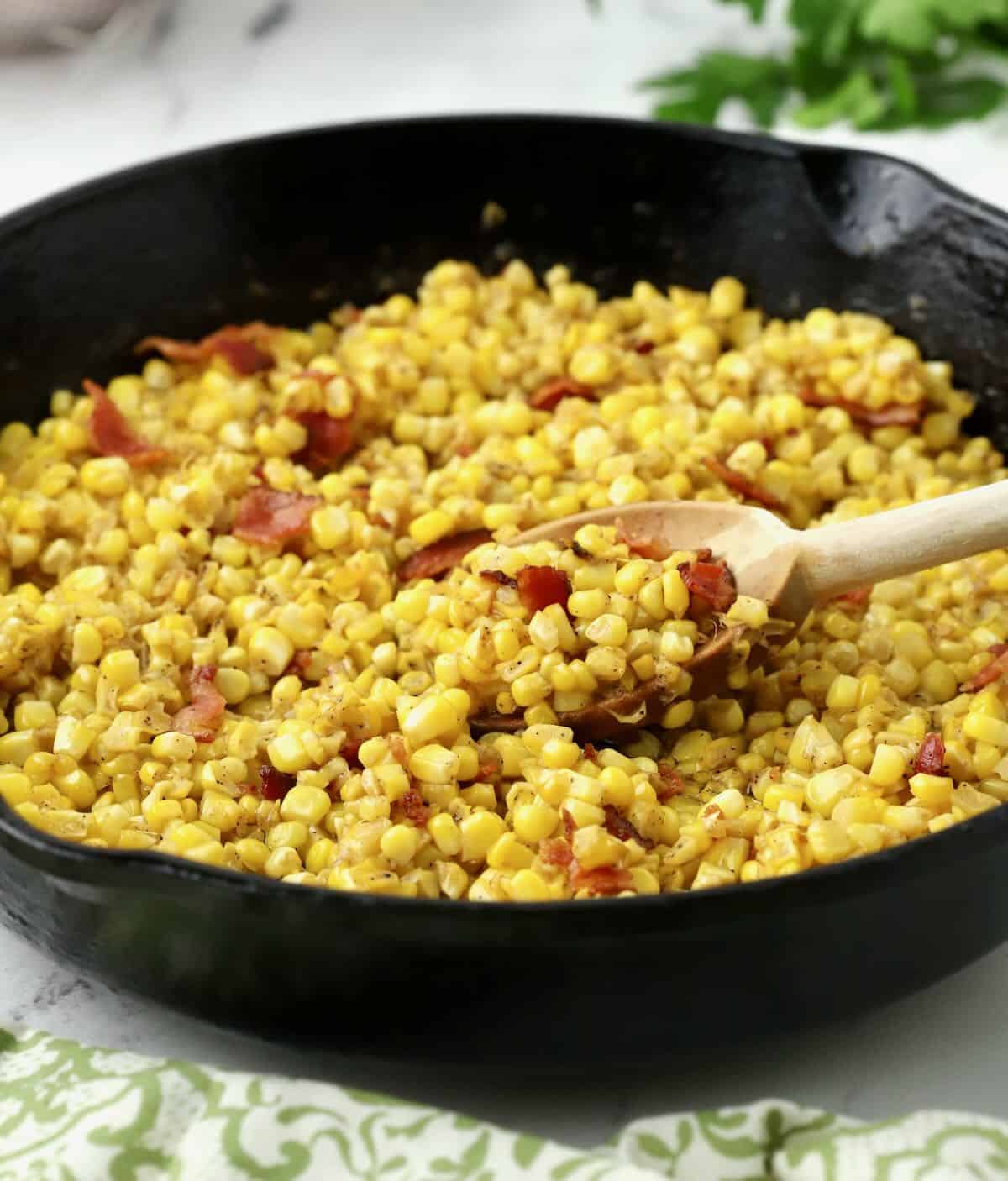 Fried corn topped with bacon in a cast iron skillet. 