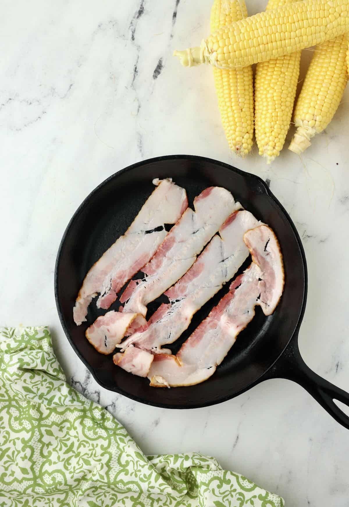 Four slices of bacon frying in a cast iron skillet. 