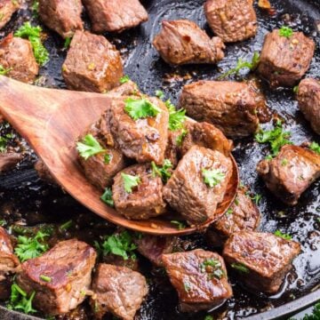 Garlic butter steak bites in a cast iron skillet with a wooden spoon.