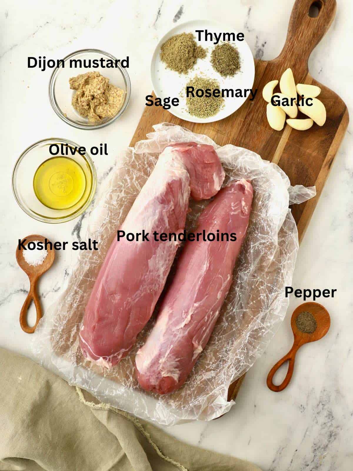 Two raw pork tenderloins, herbs, olive oil, and mustard on a cutting board. 