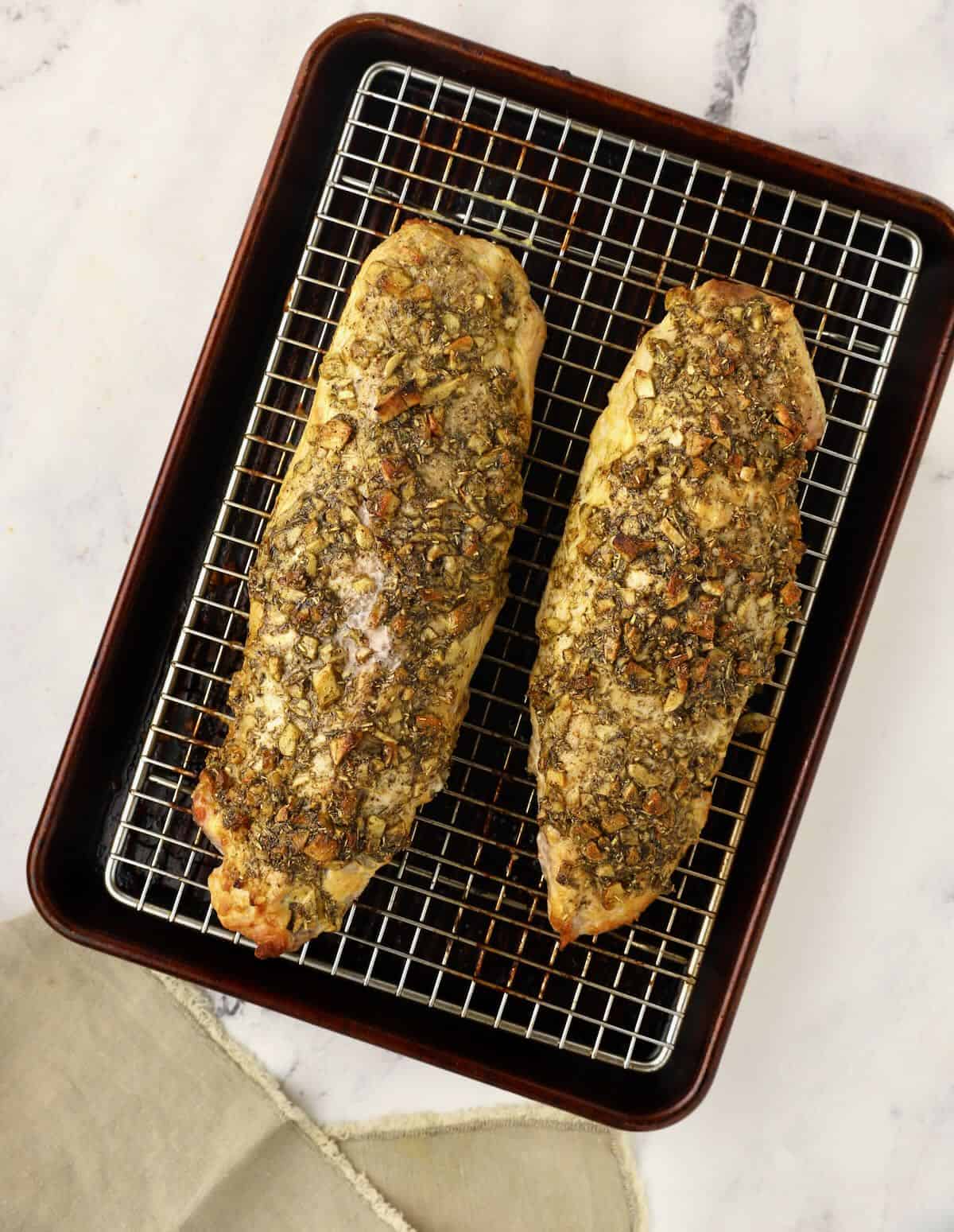 Two roasted pork tenderloins on a baking sheet just out of the oven. 