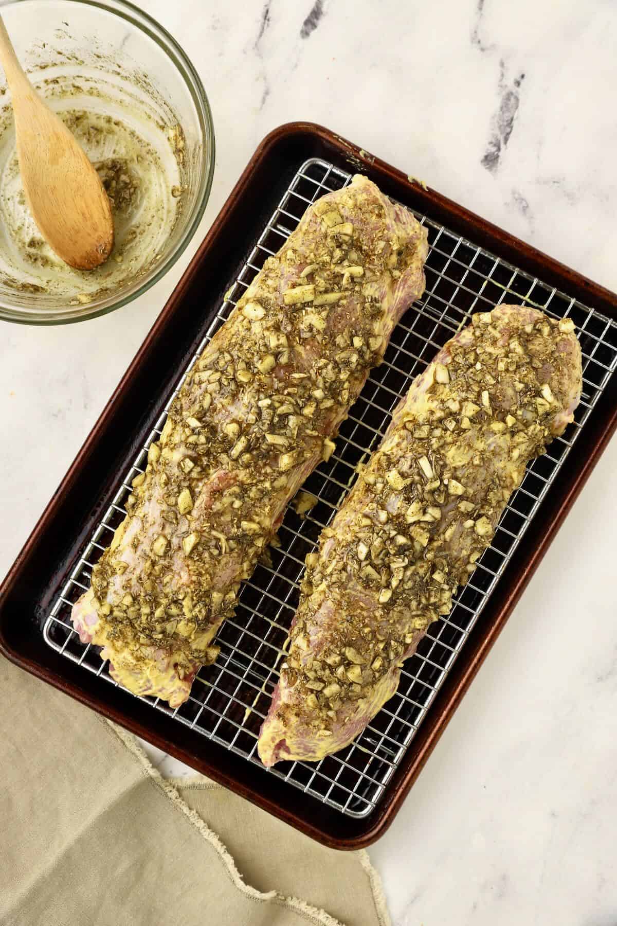 Two pork tenderloins topped with a herb and garlic mixture ready for the oven. 