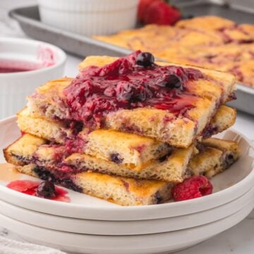 A stack of sheet pan pancakes cut into squares topped with a berry compote.