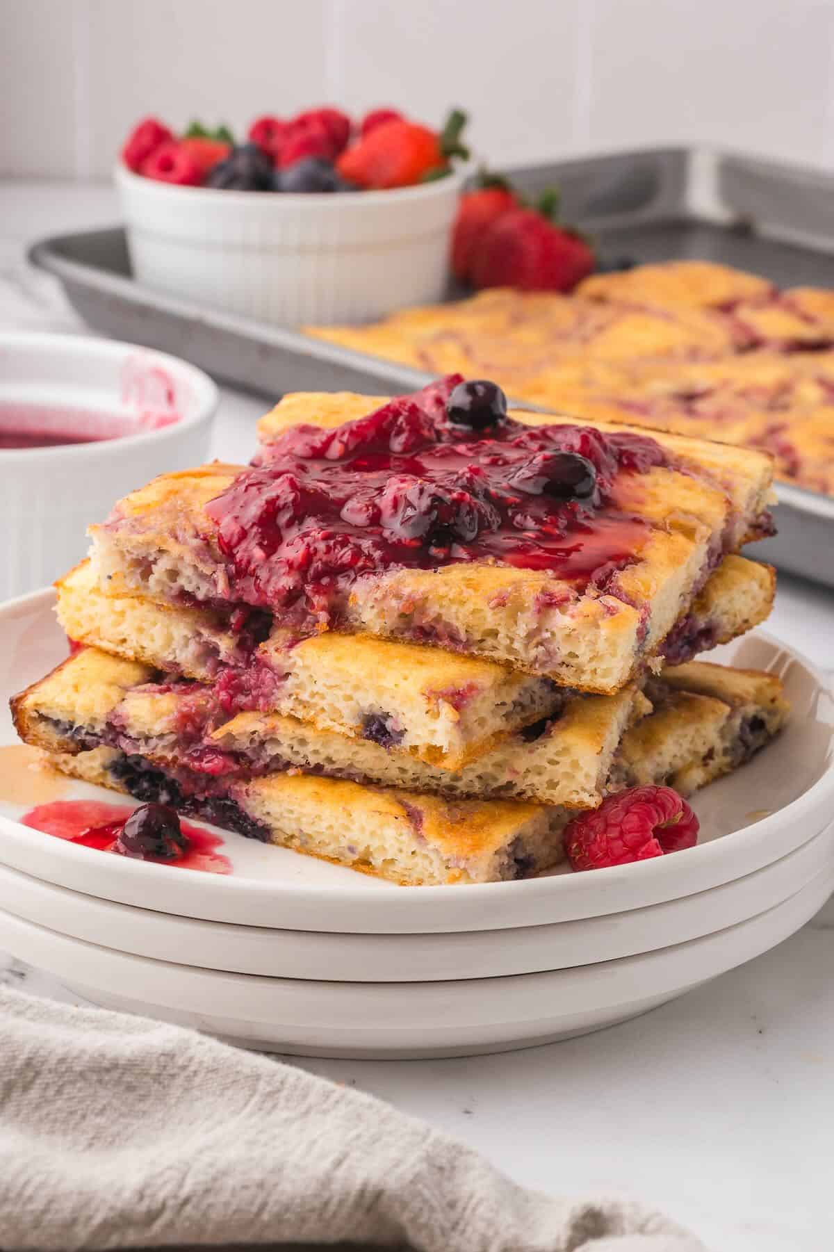 A stack of sheet pan pancakes on a white plate topped with a berry compote.