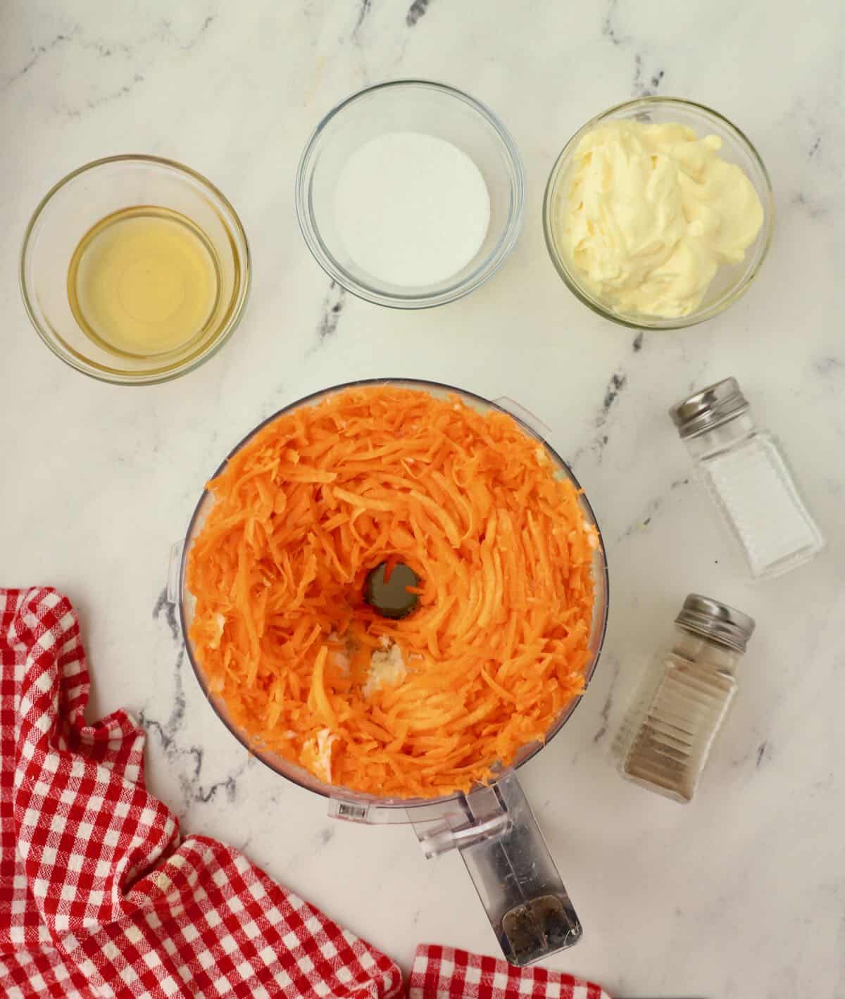 A food processor bowl with shredded carrots in it.