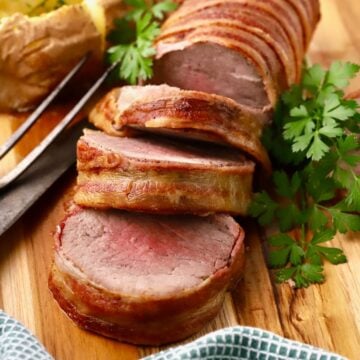 Oven roasted acon-wrapped beef tenderloin sliced on a cutting board.