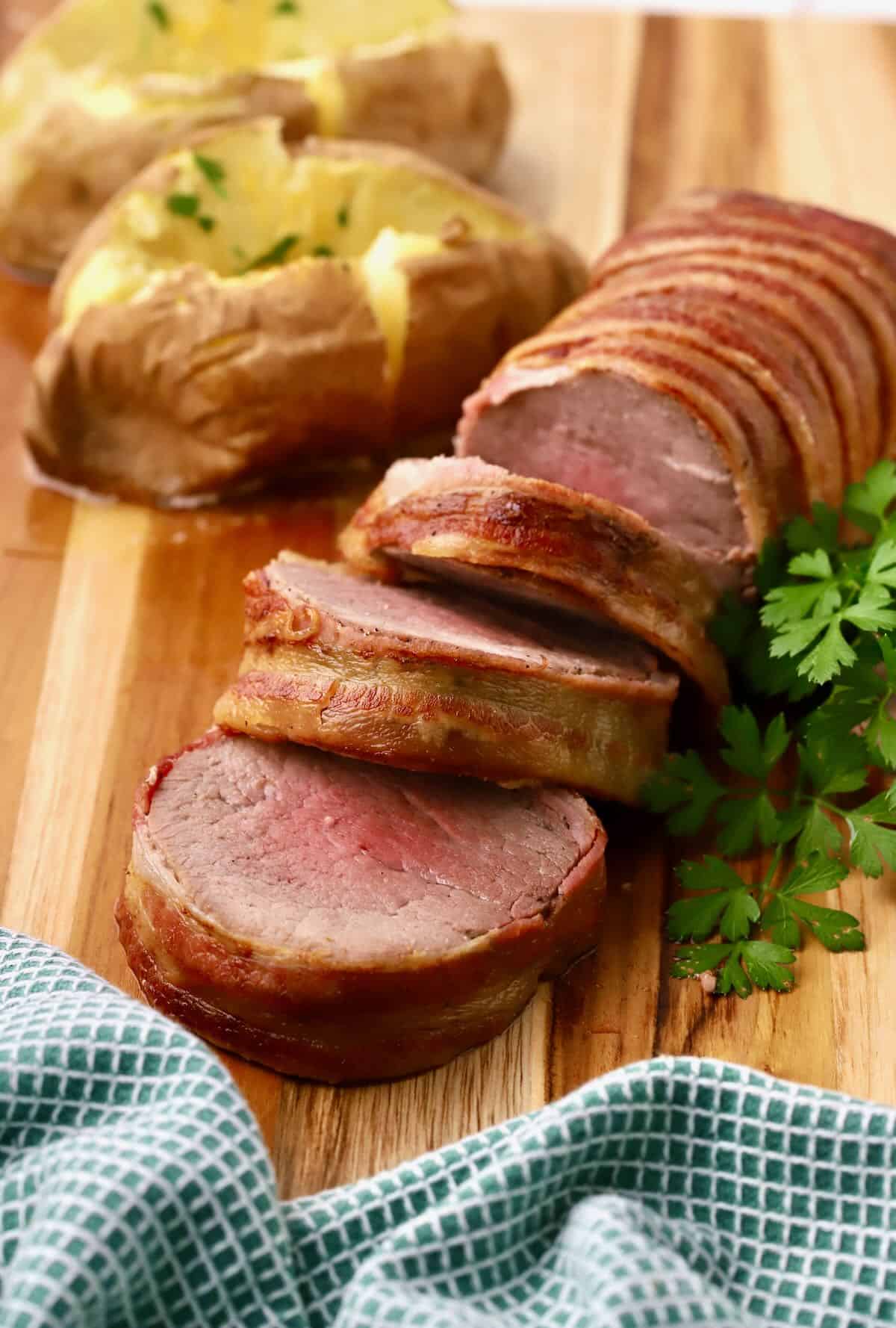 A beef tenderloin wrapped in bacon sliced on a cutting board. 