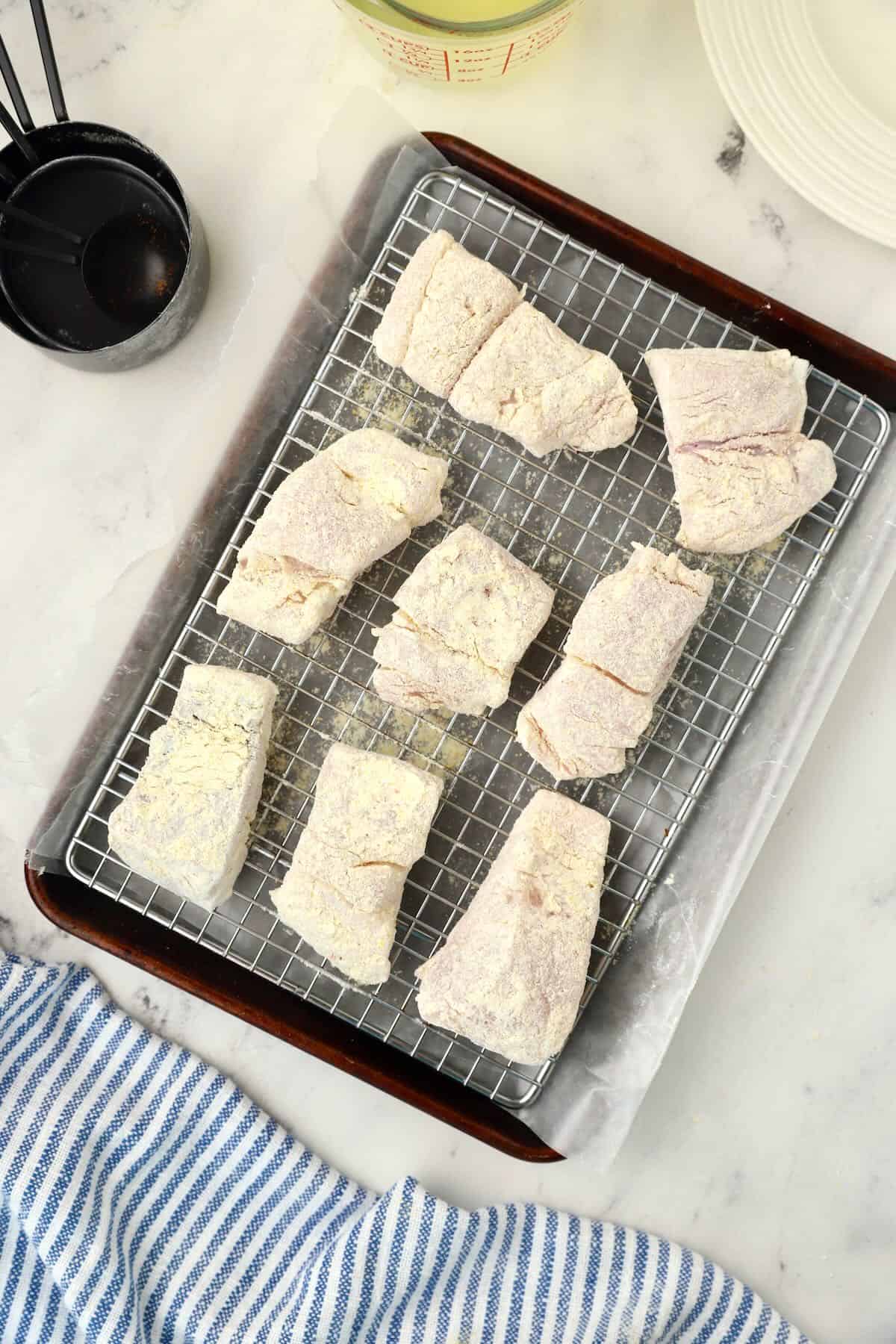 Breaded fish fillets on a wire rack over a baking sheet. 