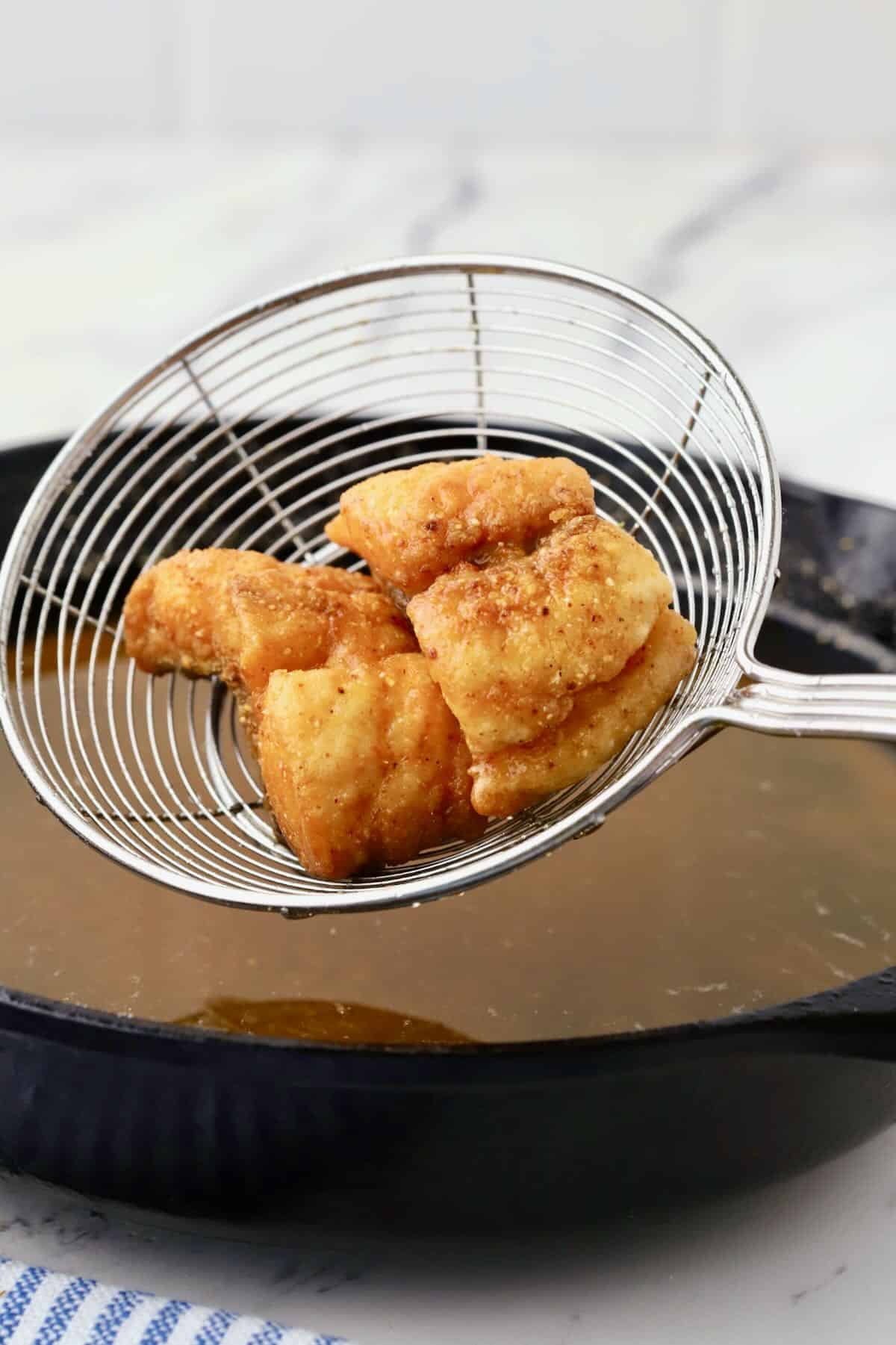 Fried red snapper bites removed from oil with a fish skimmer.