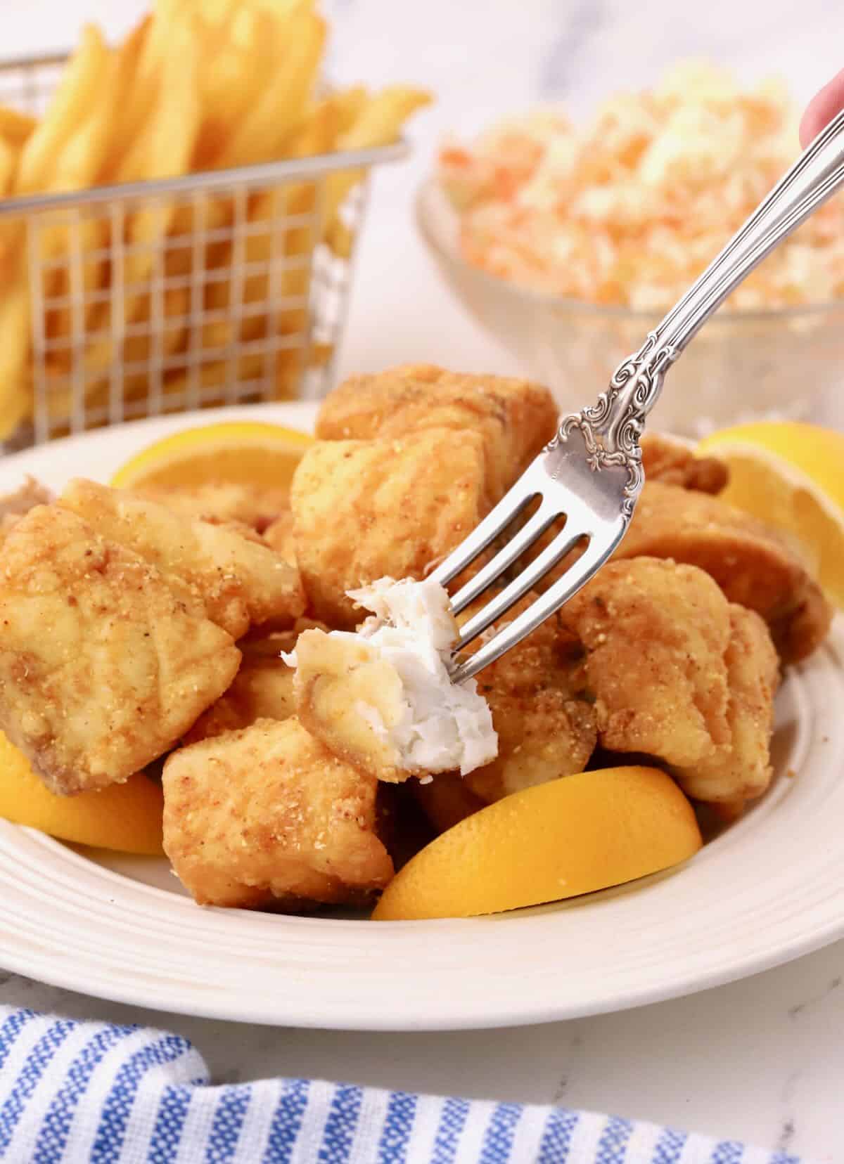 A plate full of fried red snapper bites with a fork full showing the white meat.