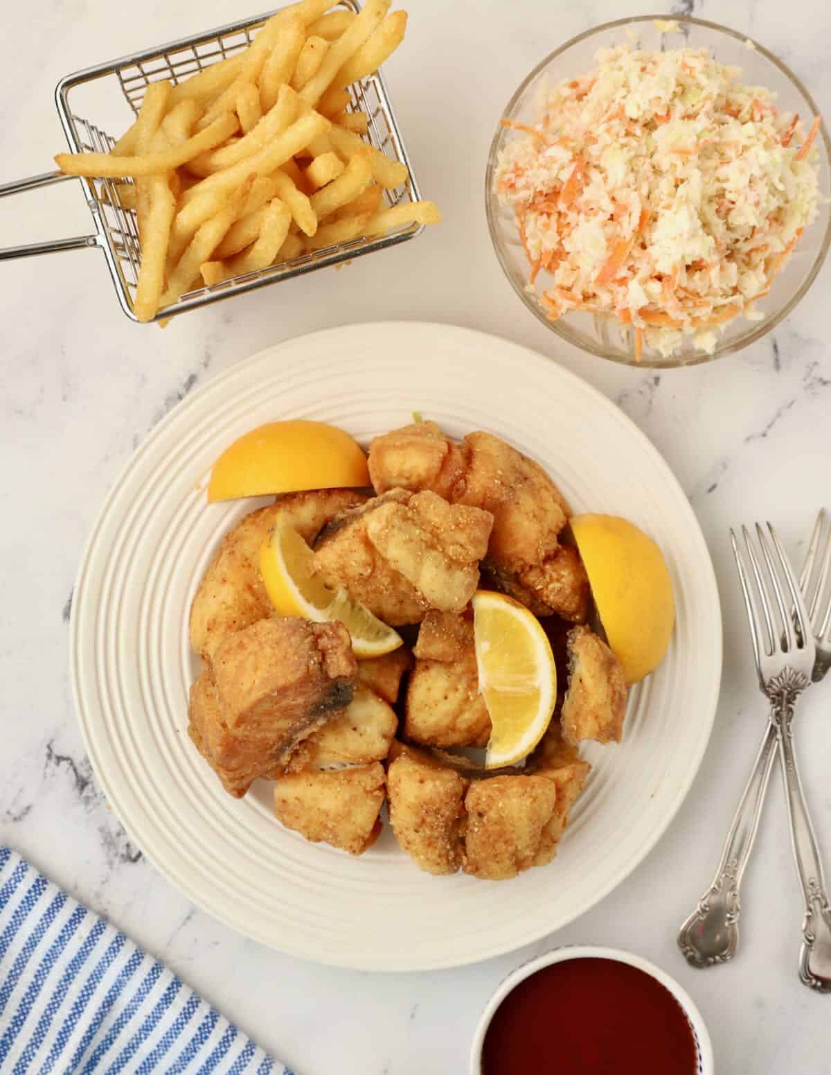 A white plate with fried snapper bites and sliced lemons. 