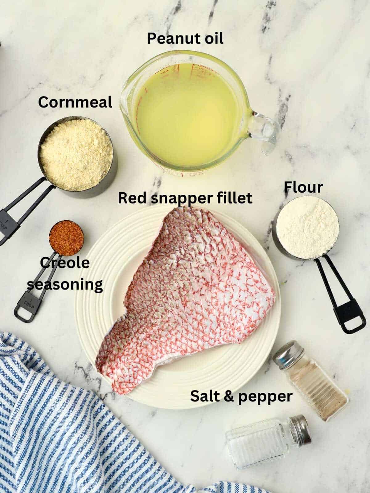 Ingredients to make fried snapper including a fish fillet, cornmeal, flour and peanut oil.