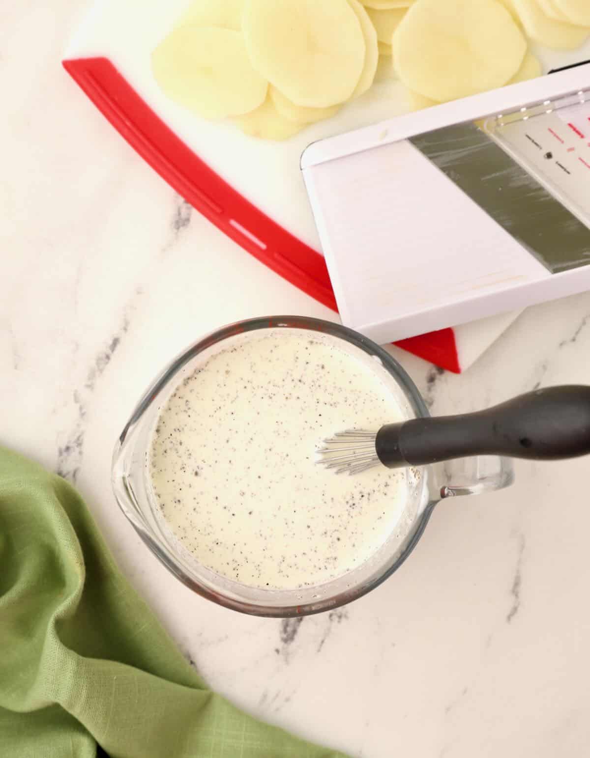 A glass measuring cup full of heavy cream with a whisk. 