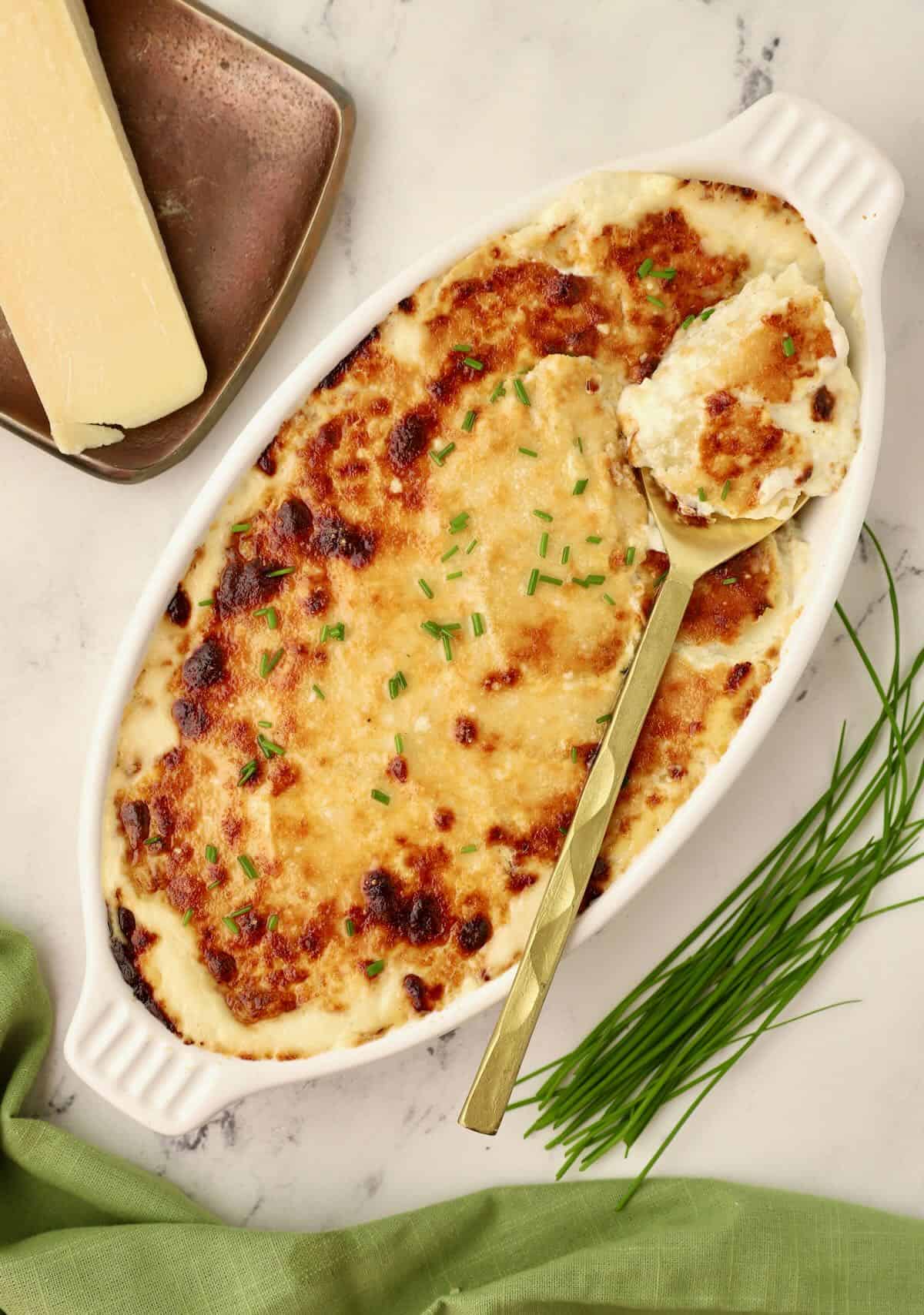 Oven-baked Potatoes Au Gratin in a white gratin dish with a gold spoon.