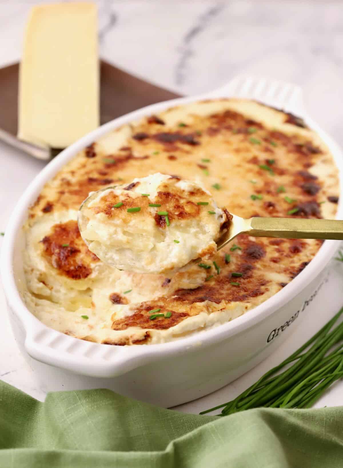 A white gratin dish full of potatoes au gratin with a spoonful taken out.