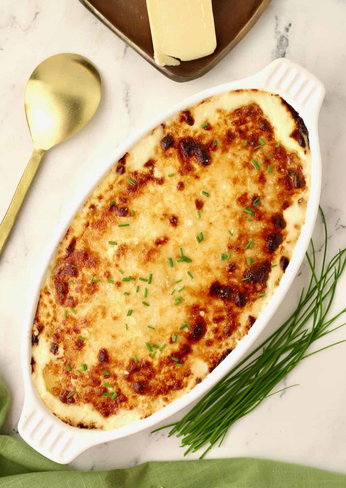 A white gratin dish with baked potatoes au gratin garnished with chives. 