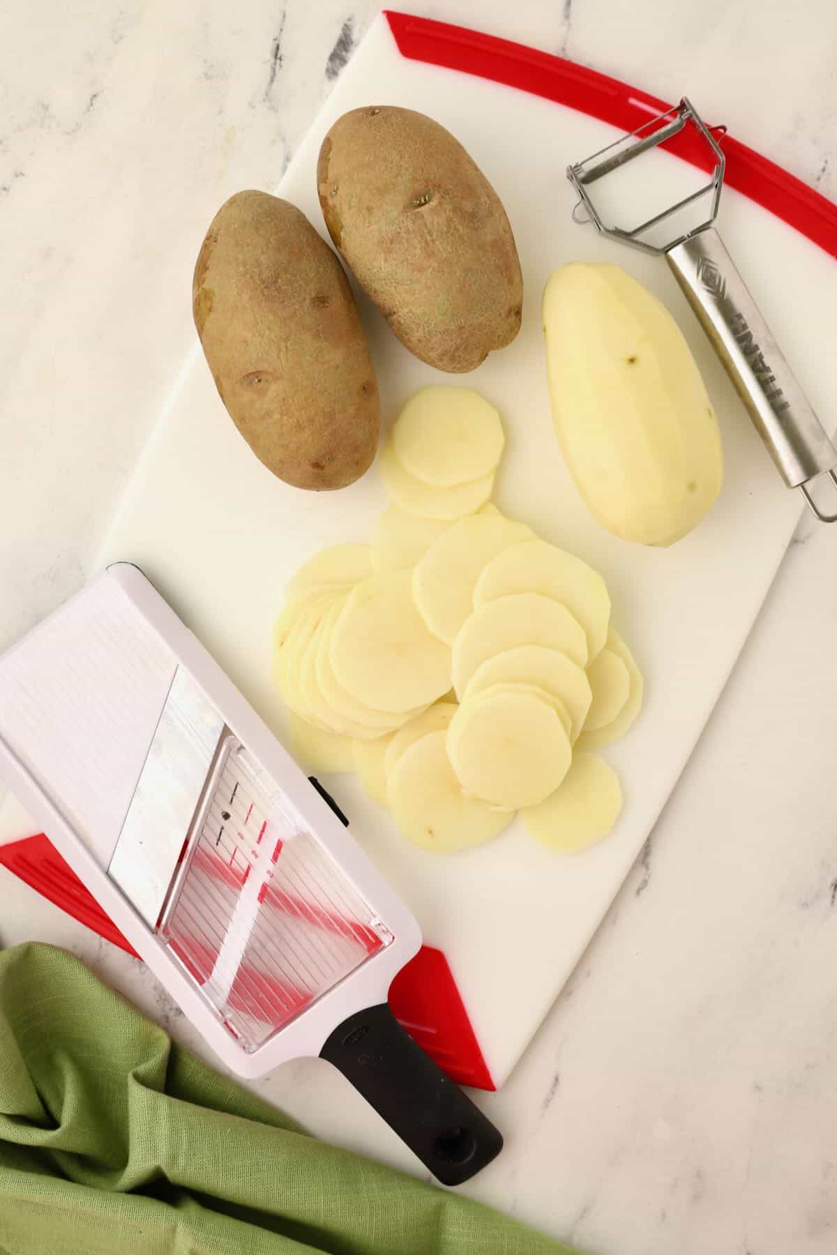 A cutting board with sliced potatoes and a mandolin.