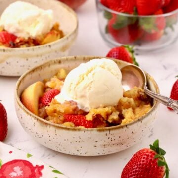 Strawberry peach cobbler in a bowl topped with a scoop of vanilla ice cream.