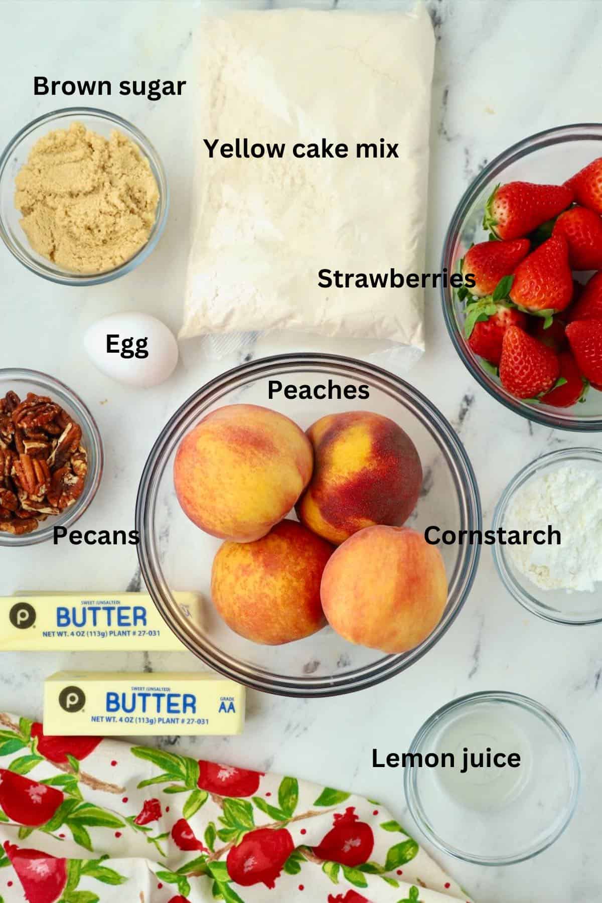 Fruit cobbler ingredients include peaches, strawberries, cake mix, and butter. 