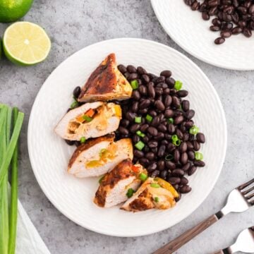 A white plate with sliced, stuffed fajita chicken breasts and black beans.