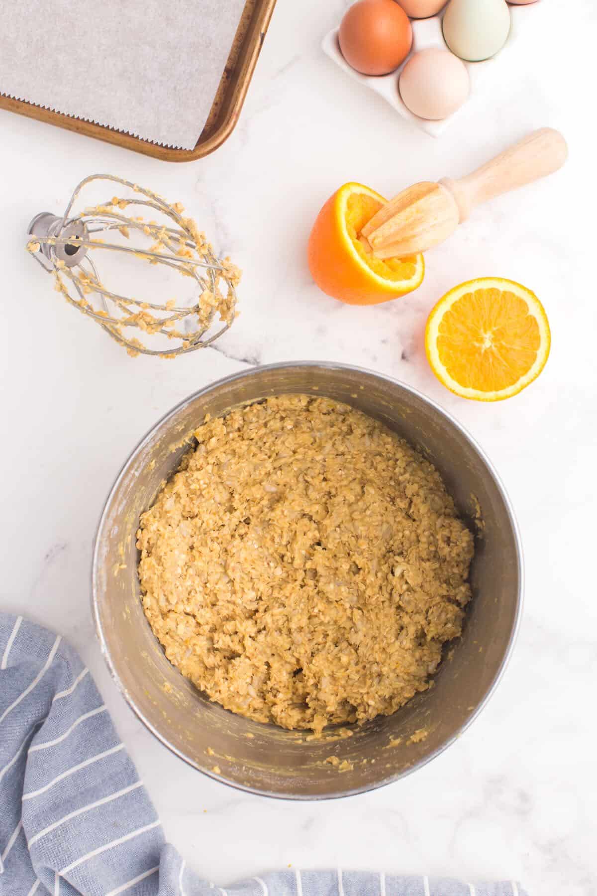 Cookie dough in a metal bowl with an orange and orange juicer next to it. 