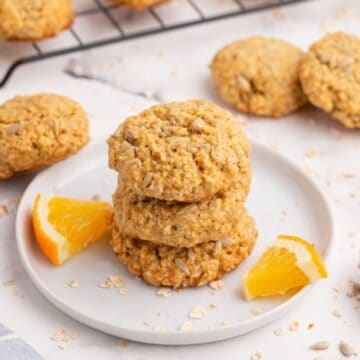 Sunflower seed cookies stacked on a white plate with fresh orange slices.