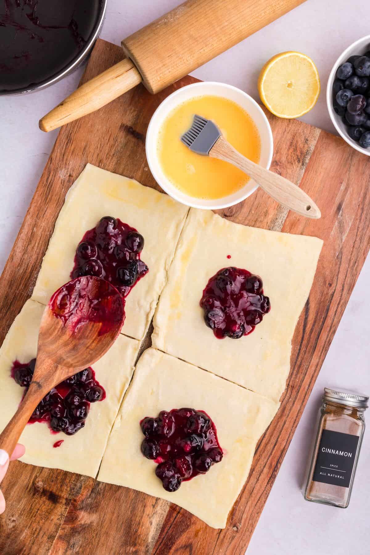 Adding a small amount of blueberry filling to puff pastry squares. 