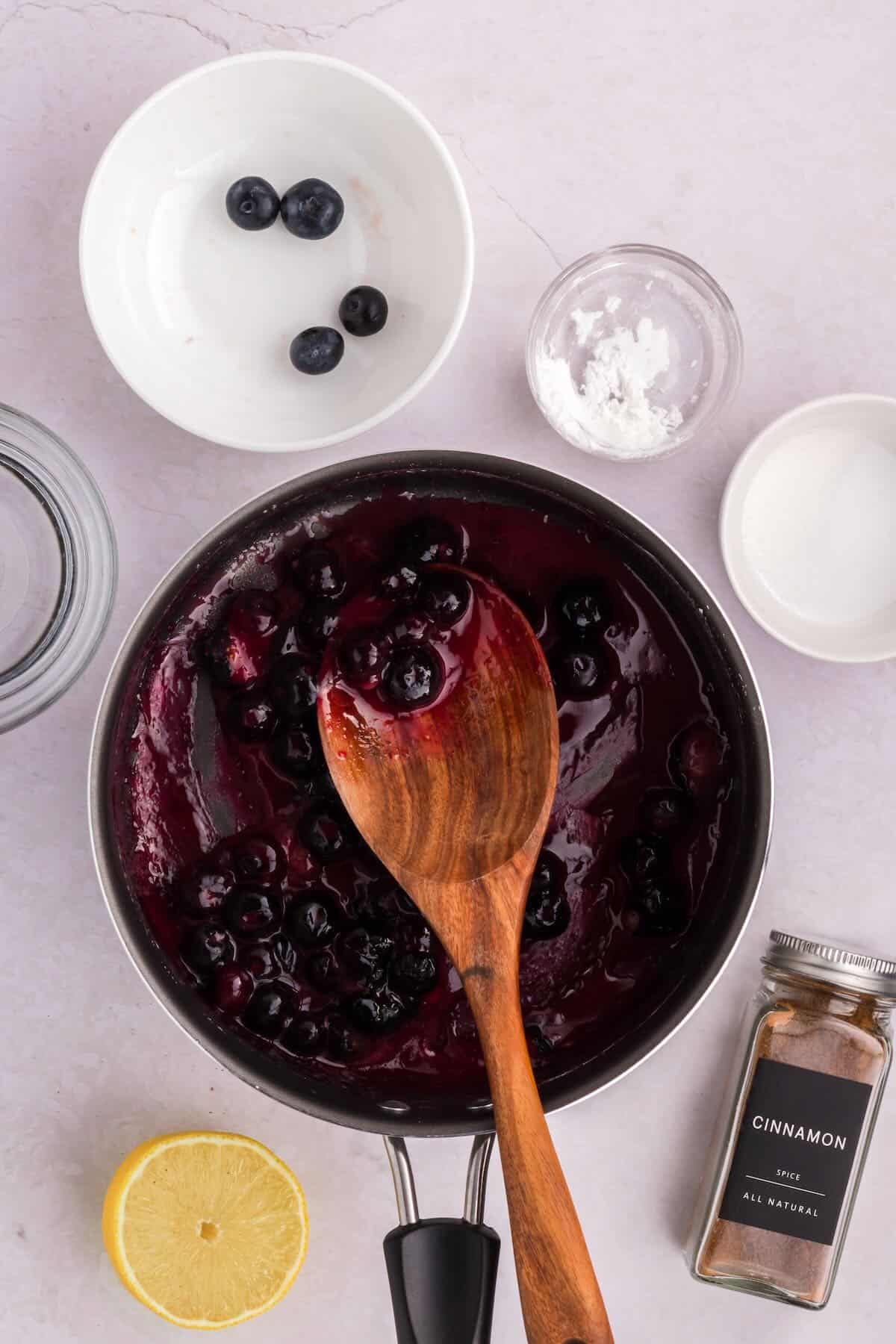 Blueberry filling cooking in a skillet with a wooden spoon. 