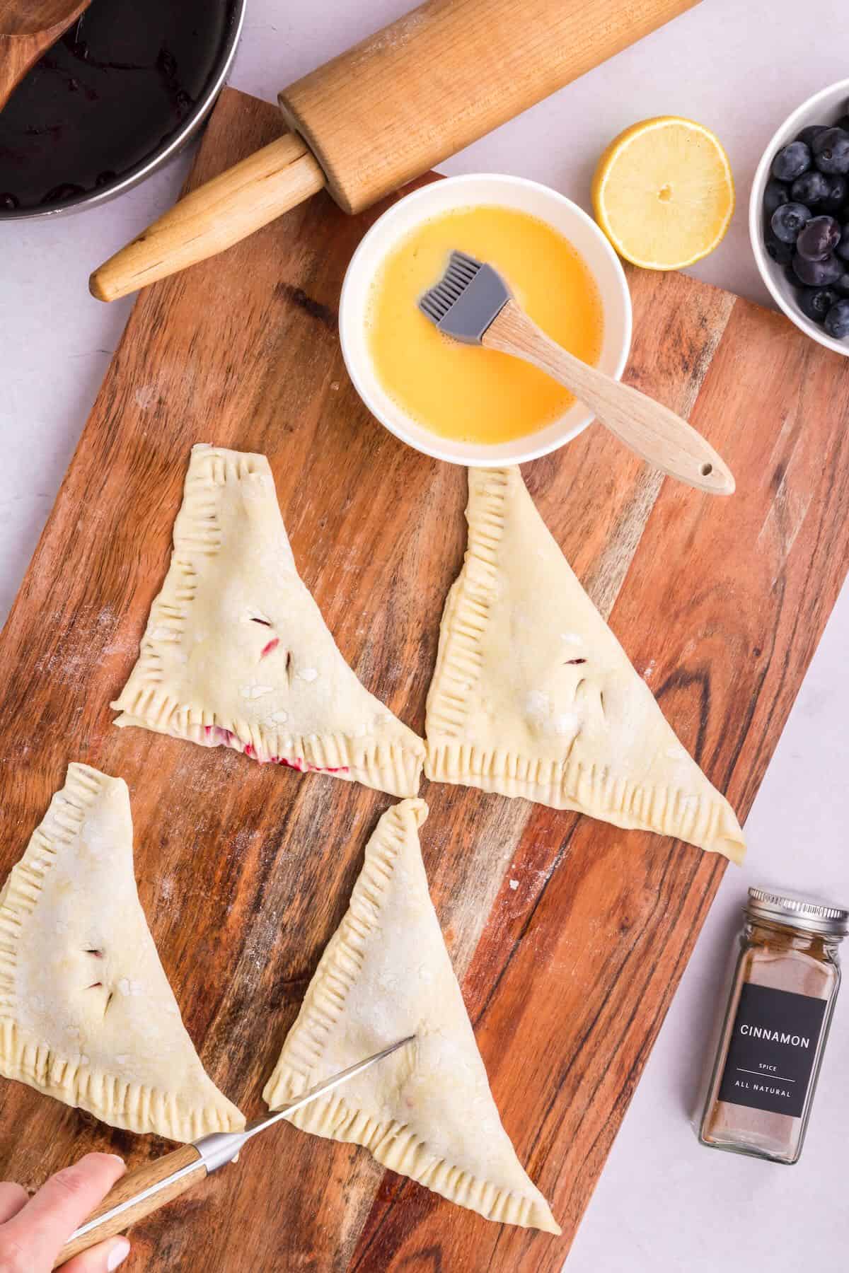 Unbaked blueberry turnovers with the raw dough edges sealed and cuts in the top so the steam can escape. 