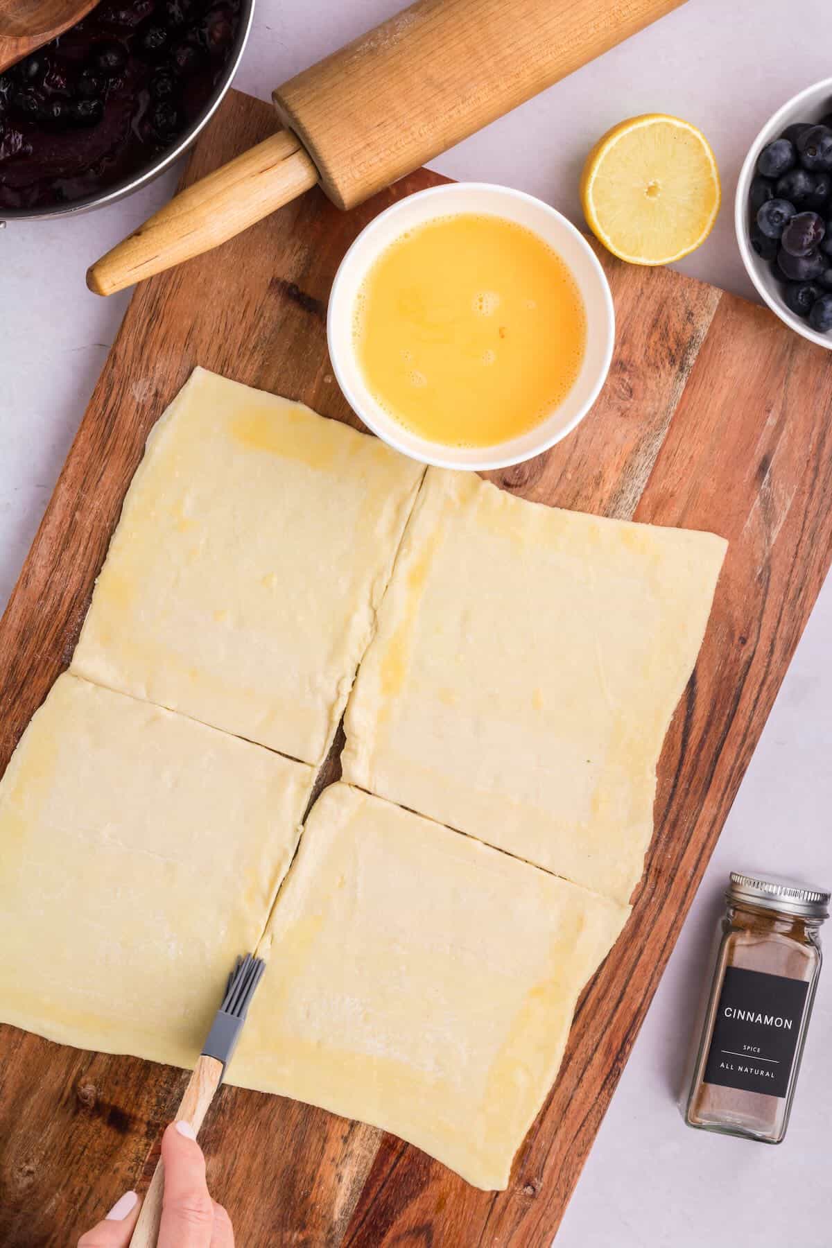 Using a pastry brush to apply egg wash to the edges of puff pastry squares. 