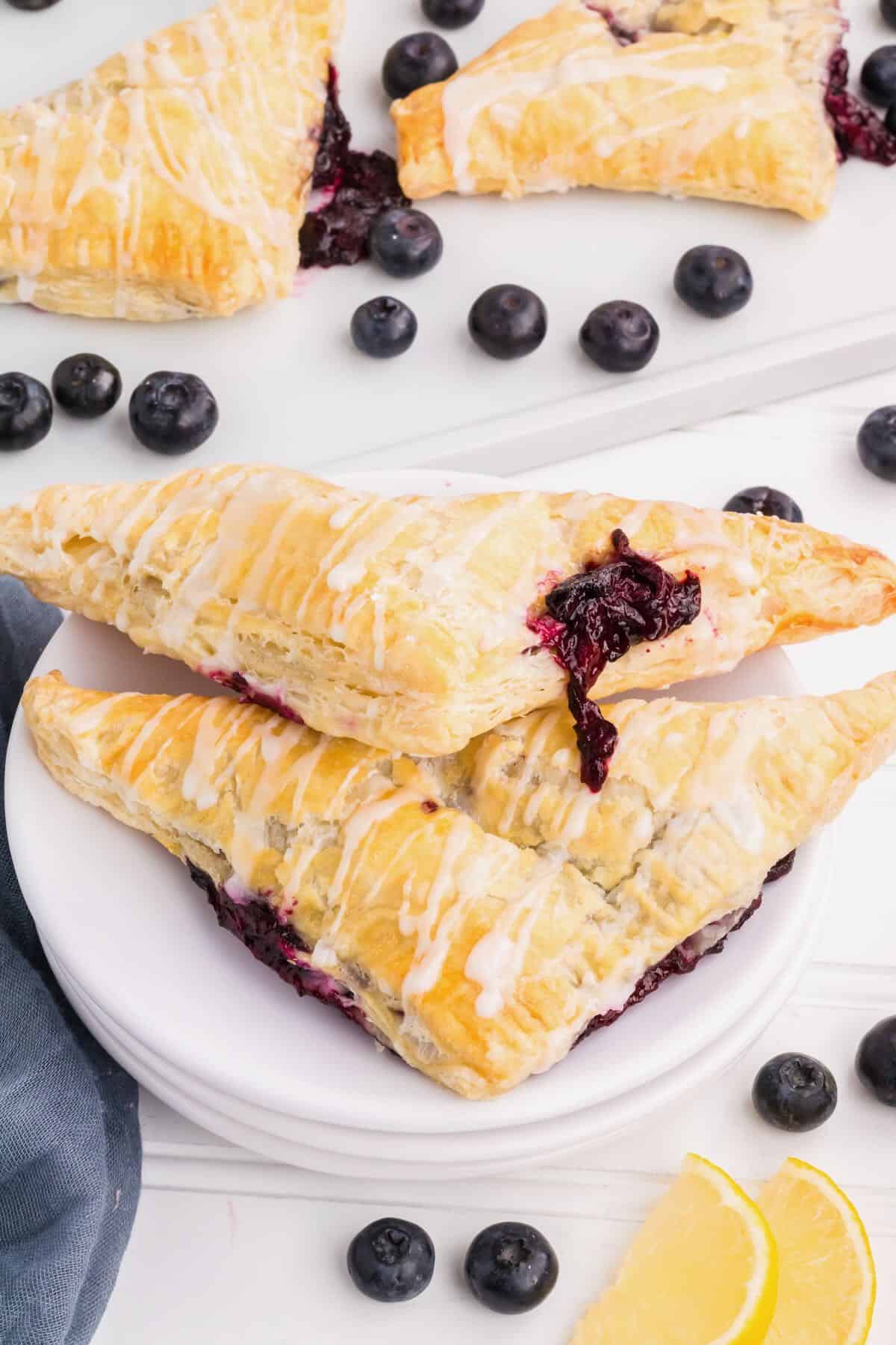 Two blueberry turnovers with a bit of blueberry filling oozing out on a white plate