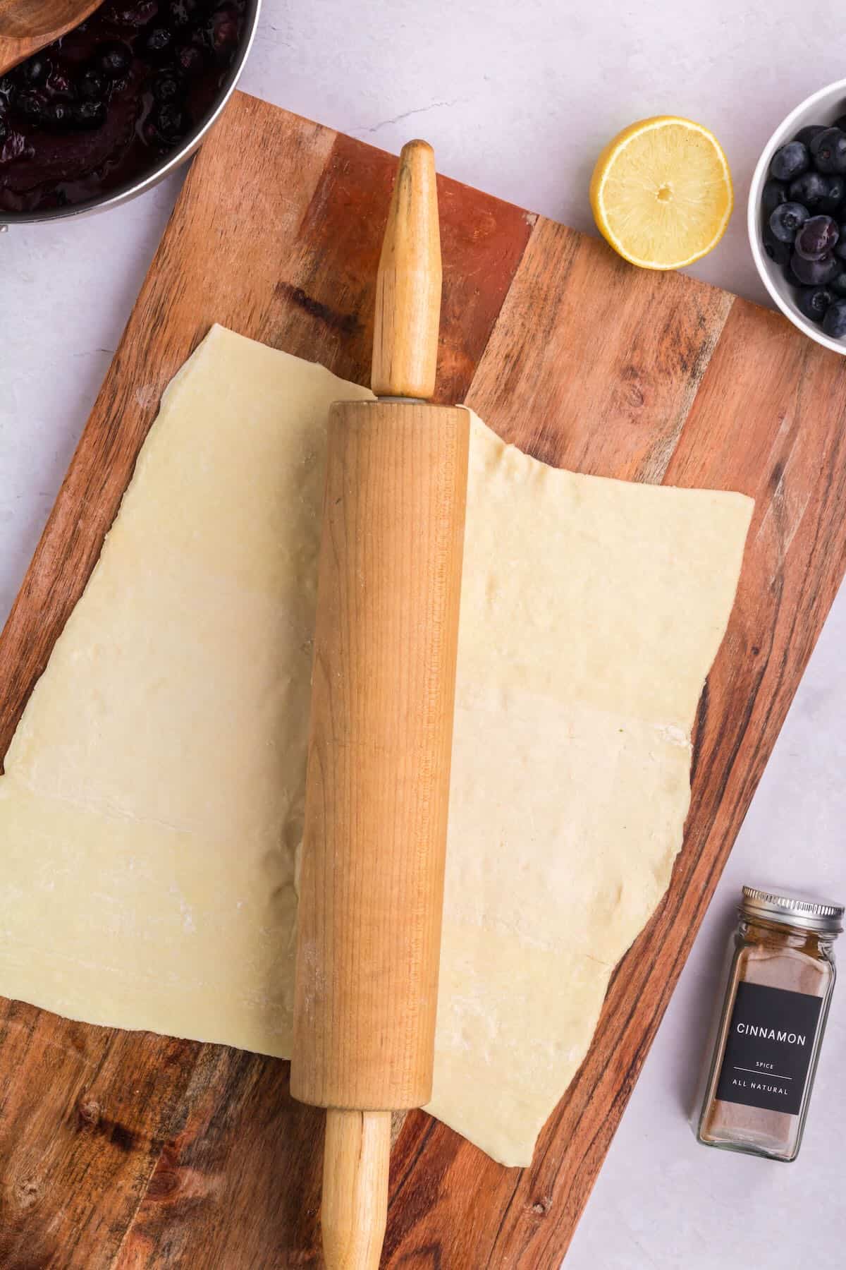 A piece of puff pastry on a cutting board with a rolling pin. 