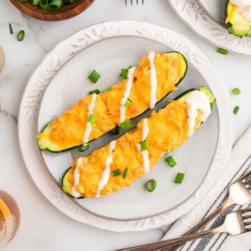 Two buffalo chicken zucchini board on a white plate garnished with sour cream and chopped scallions.