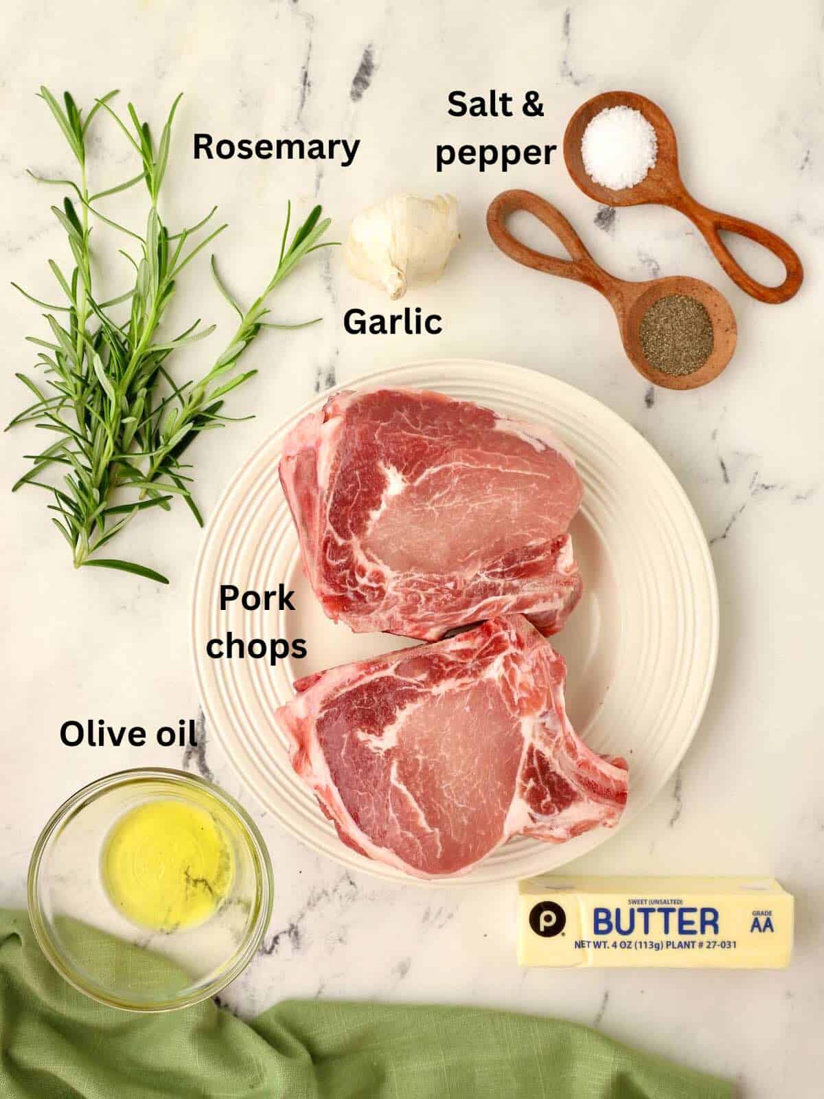 Pork chops, rosemary, a garlic bulb, and salt and pepper on a cutting board to make Rosemary Pork Chops. 