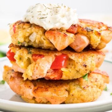 Three salmon patties stacked on a plate with a dollop of aioli on top.