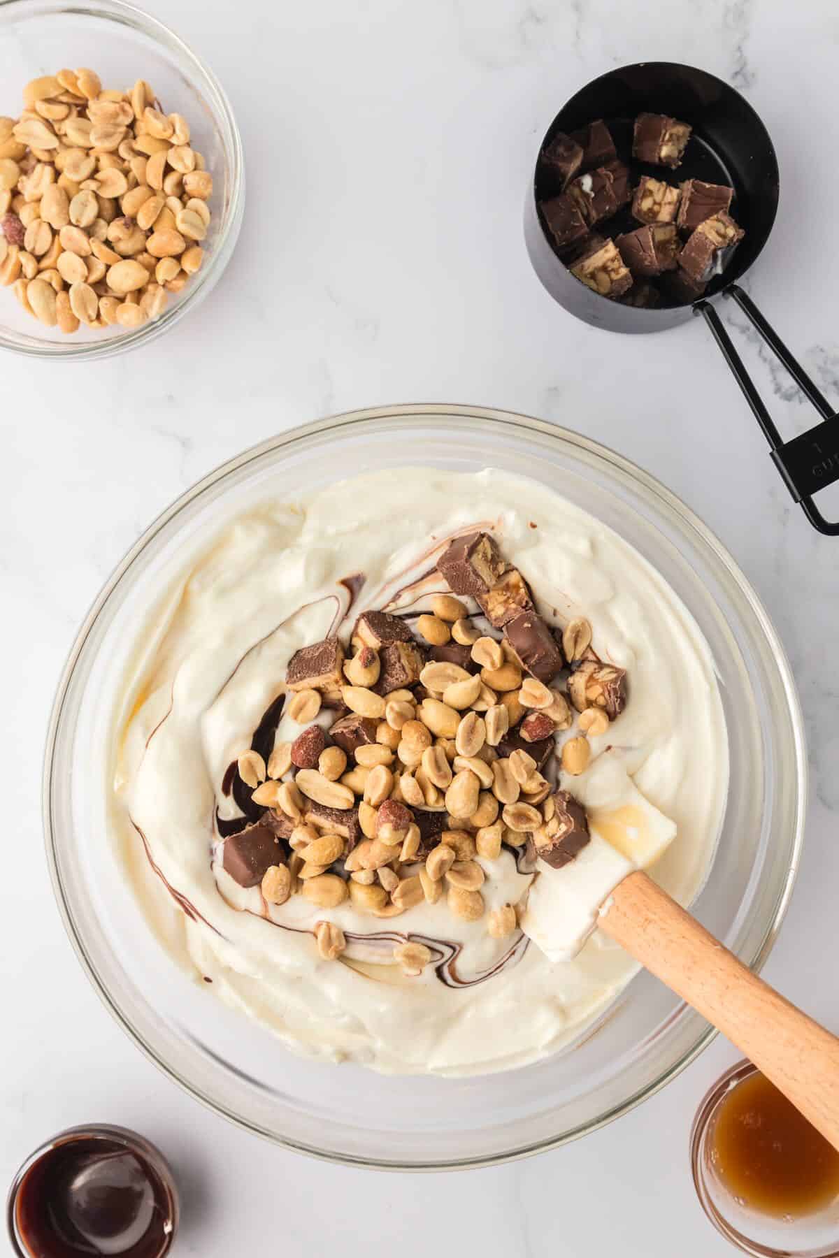Whipped cream, condensed milk, chocolate sauce, and peanuts in a bowl. 