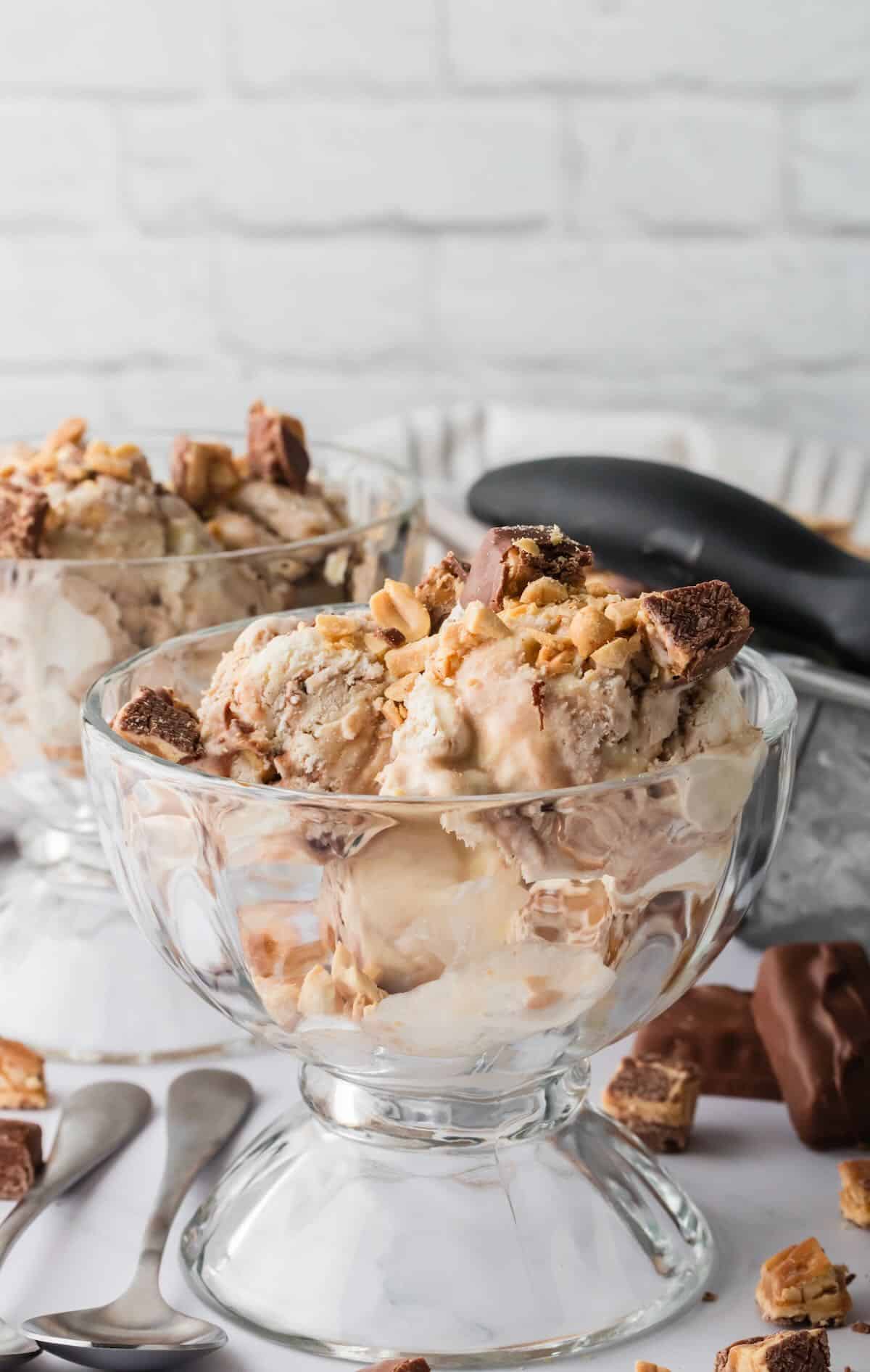 A clear glass dessert dish full of snickers ice cream. 