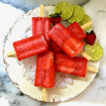 Six frozen strawberry margarita ice pops on a plate full of ice.