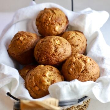 A basked full of apple cranberry muffins with a white napkin under them.