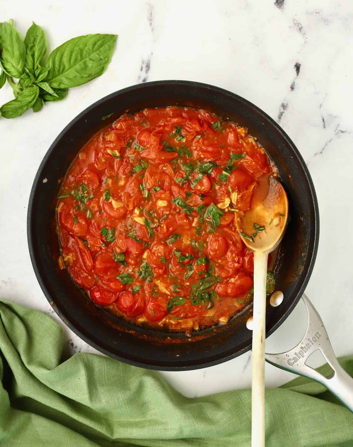 Cherry tomato sauce with basil cooking in a skillet. 